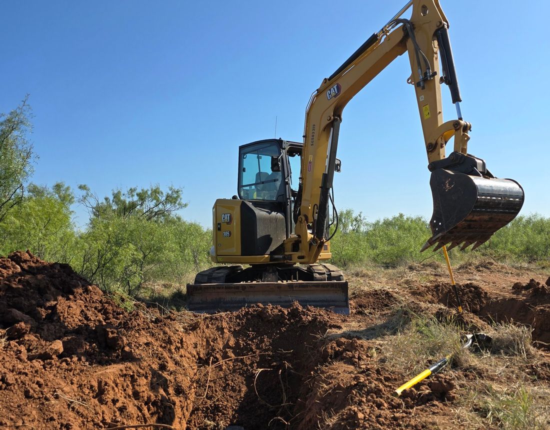 Excavator trenching in red dirt on a West Texas jobsite
